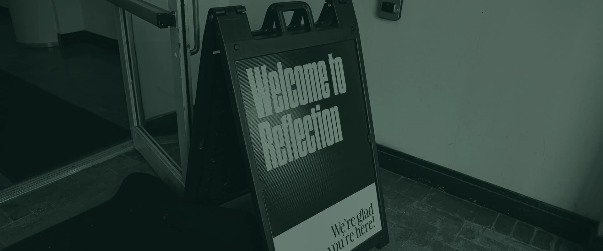 A-frame sign outside the entrance reading Welcome to Reflection, we're glad you're here